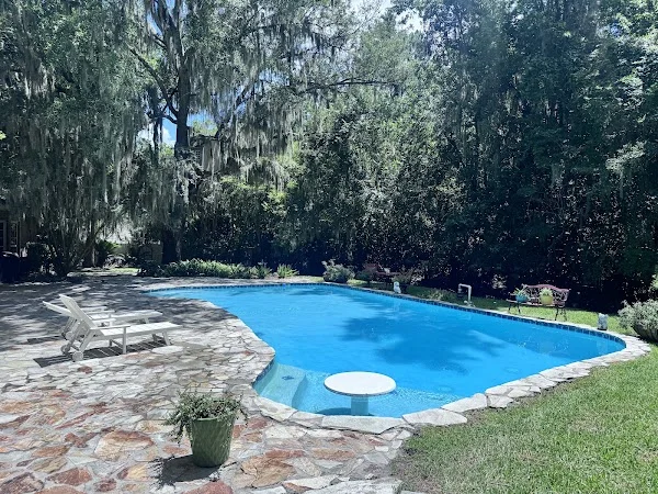 Clear blue backyard pool surrounded by stone paving and trees